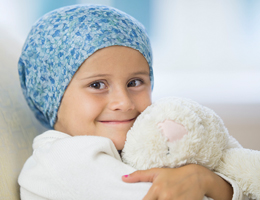 A smiling child wearing a head scarf hugs a stuffed animal.