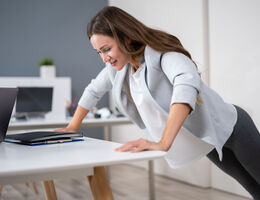 A woman does a pushup against the edge of her desk.